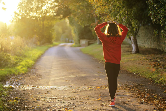 A woman is walking alone down a sunny country road.