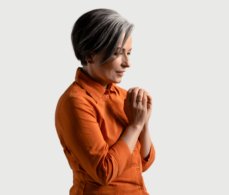 Woman in orange top with head tilted down and hands in praying position.